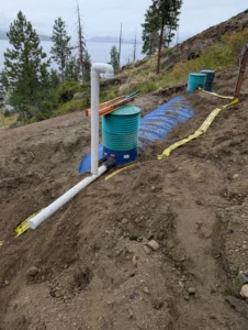 Completed Type 2 septic system installation on a steep hillside, featuring green access riser lids, proper PVC venting, and safety grading overlooking Okanagan Lake.