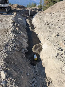 Excavation of a standard gravity septic trench featuring a gravel bed and inspection port on a rocky hillside property in the Okanagan.